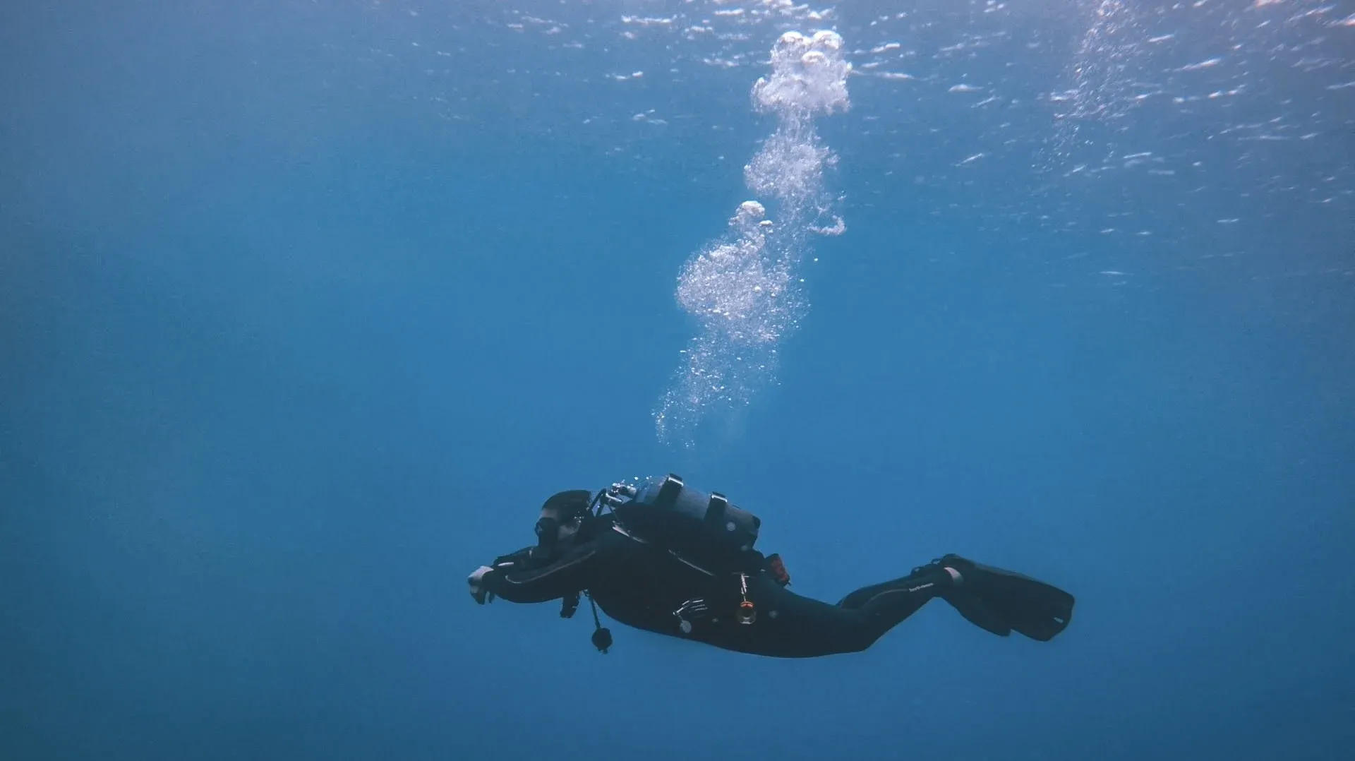 A diver suspended in open blue water, exhaled bubbles rising to the surface